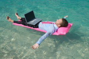 Genç bir çalışan iş seyahatinde dizüstü bilgisayarıyla çalışıyor; iş ve tatil dengesi temalı görsel.