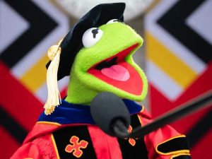 Kermit the Frog, cübbe ve kep giymiş şekilde bir mezuniyet töreninde konuşma yapıyor.