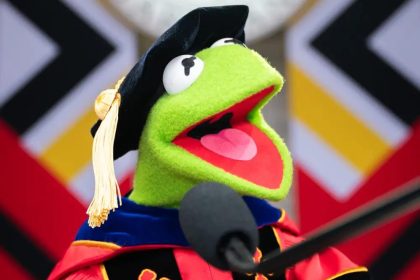 Kermit the Frog, cübbe ve kep giymiş şekilde bir mezuniyet töreninde konuşma yapıyor.