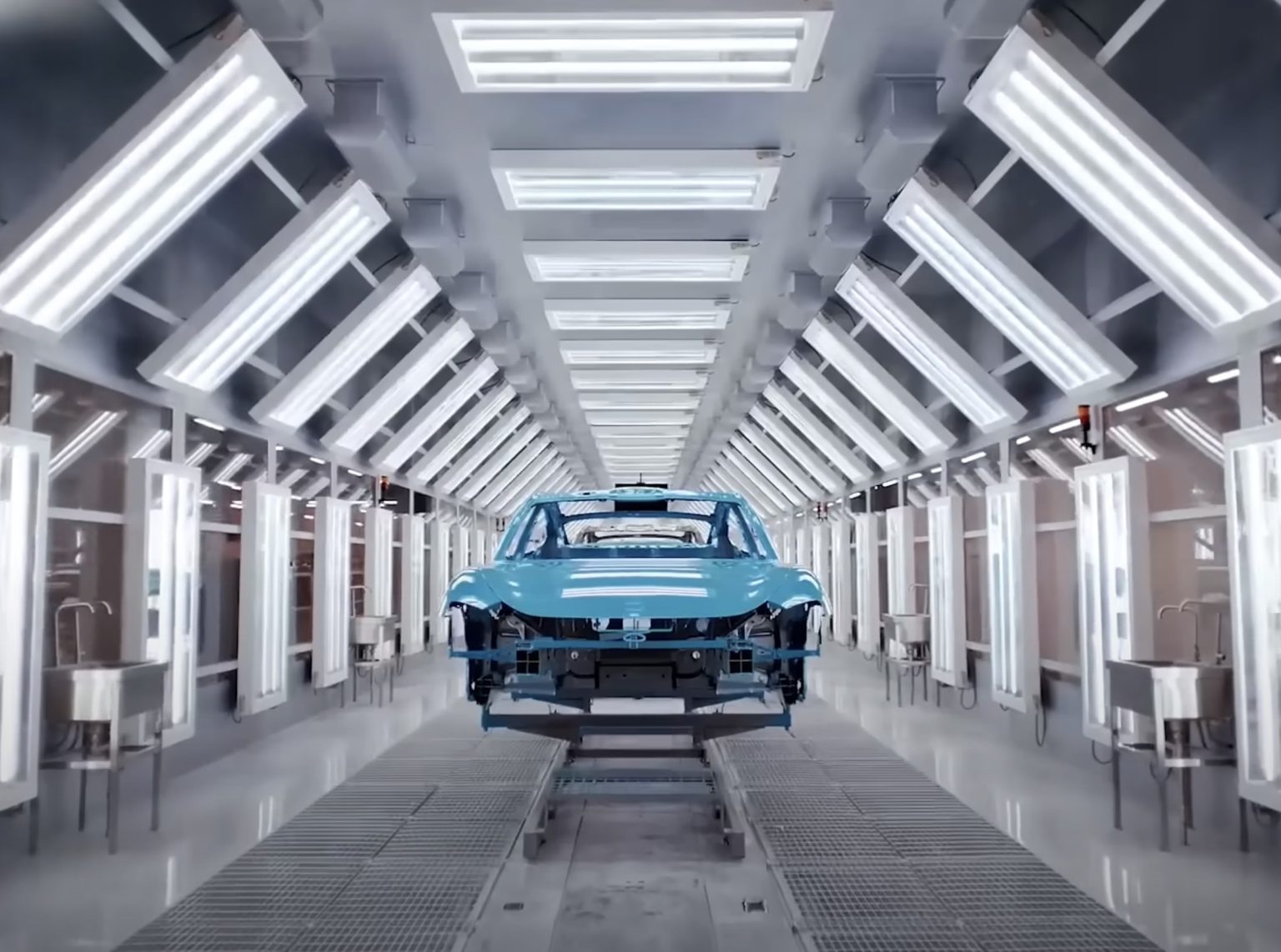 Xiaomi fabrikasında otomasyonla üretilen elektrikli araçların montaj hattını gösteren geniş açılı bir üretim bandı fotoğrafı; yüksek hızlı robotlar, parlak zeminli fabrika ortamı ve SU7 model araçlar üretim bandında ilerliyor.