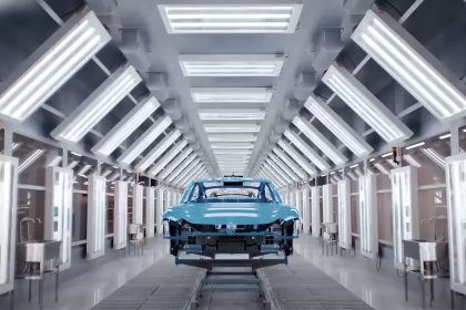 Xiaomi fabrikasında otomasyonla üretilen elektrikli araçların montaj hattını gösteren geniş açılı bir üretim bandı fotoğrafı; yüksek hızlı robotlar, parlak zeminli fabrika ortamı ve SU7 model araçlar üretim bandında ilerliyor.